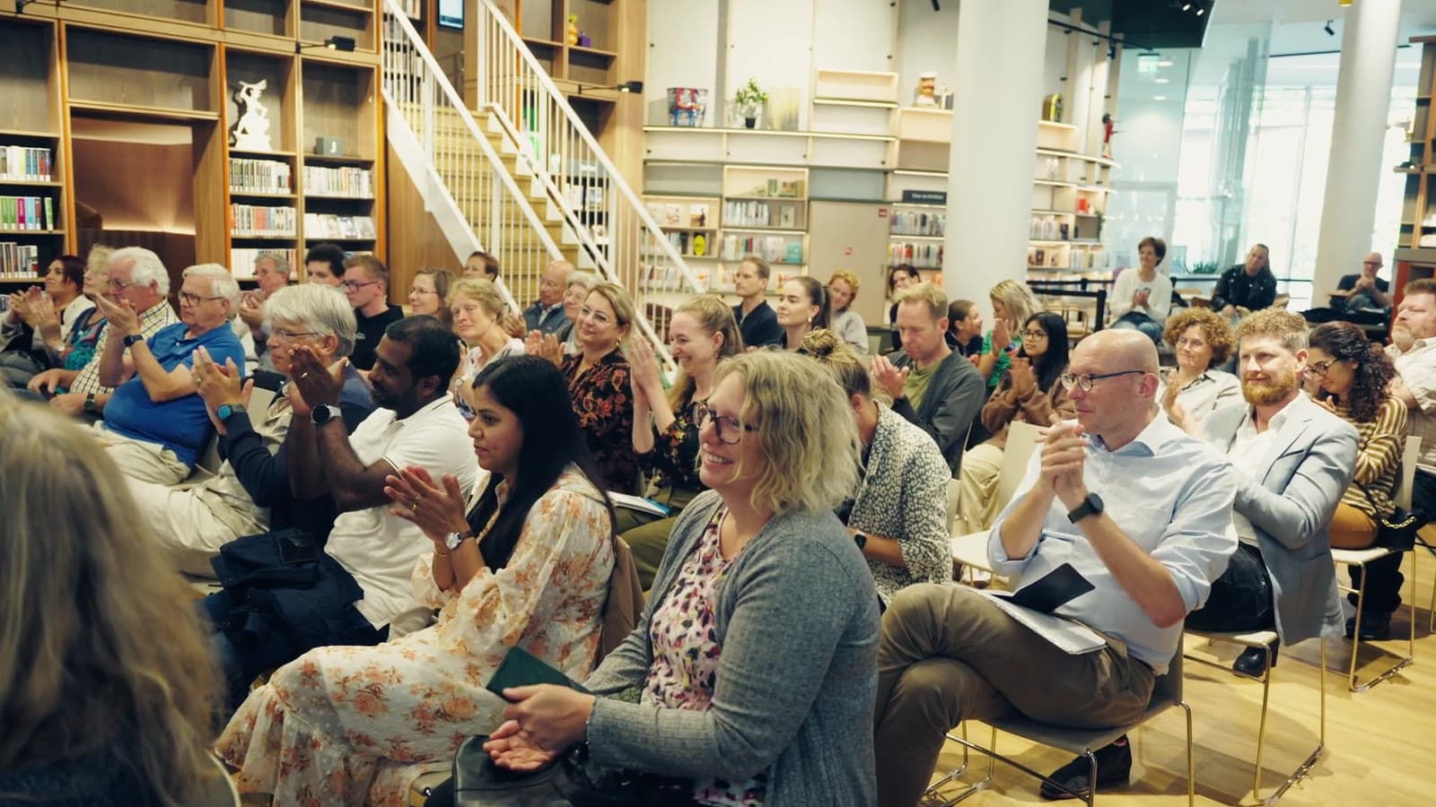 Publiek applaudisseert tussen de boekenkasten, still uit de aftermovie van de Ideeënmarkt 2024 voor jongeren in Nieuwegein