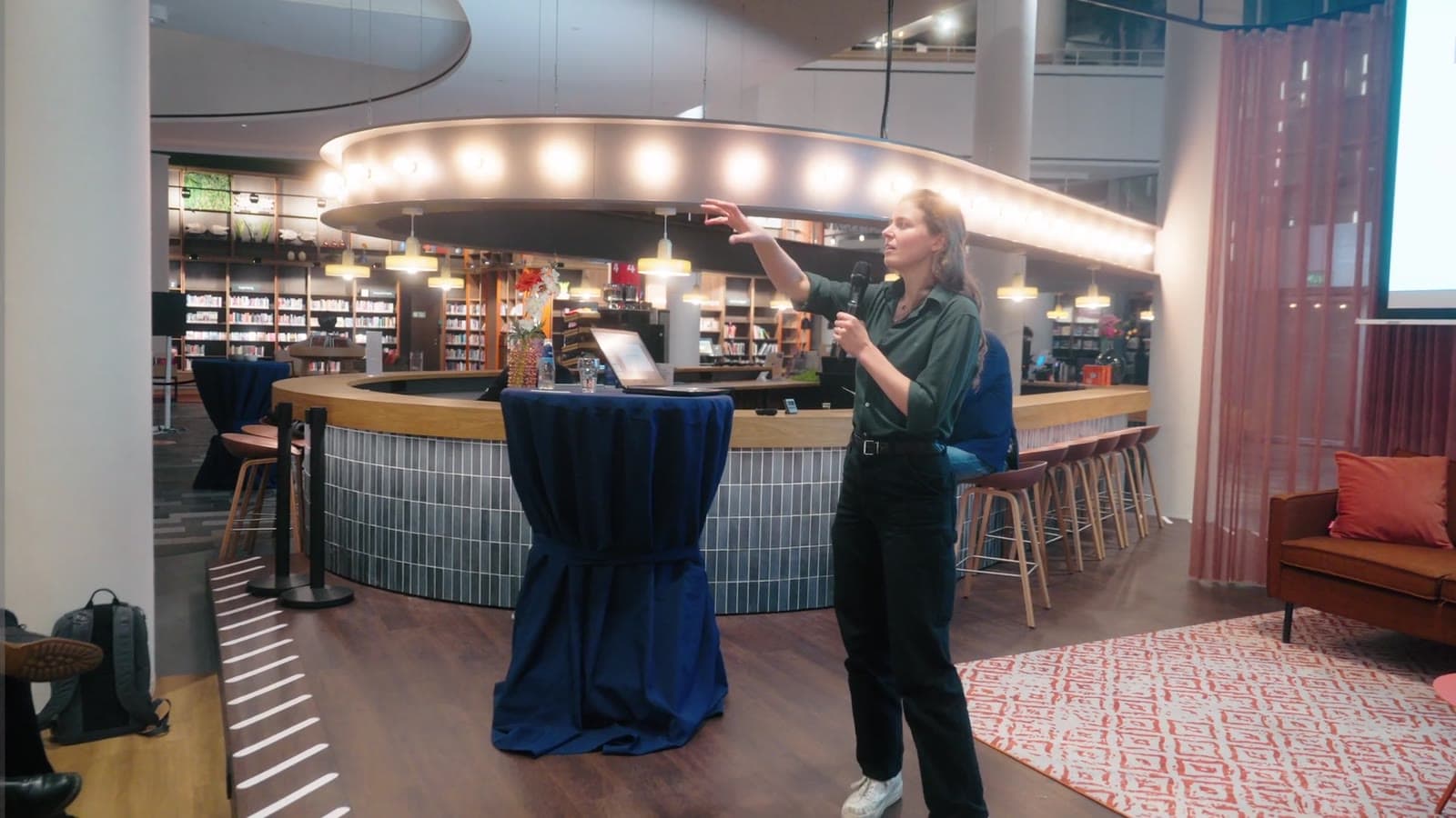 Een vrouw presenteert met een microfoon haar idee aan het publiek, still uit de aftermovie van de Ideeënmarkt 2025 in Nieuwegein